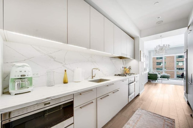 kitchen featuring a sink, light wood-style floors, decorative backsplash, white oven, and white cabinets