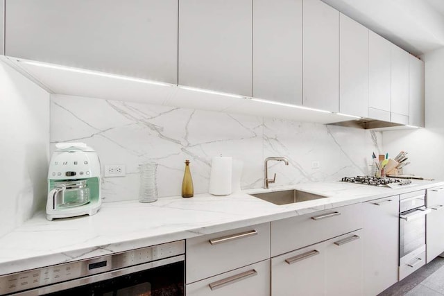 kitchen featuring a sink, oven, backsplash, gas cooktop, and light stone countertops