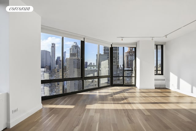 304 E 65th St Unit 26B, New York City, NY 10065 - spare room featuring a skyline view, wood finished floors, radiator heating unit, baseboards, and rail lighting