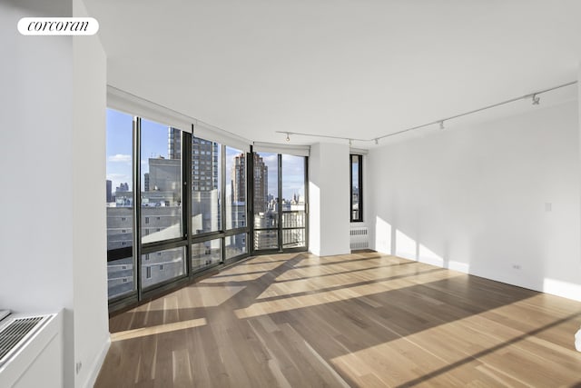 304 E 65th St Unit 26B, New York City, NY 10065 - unfurnished room with radiator heating unit, rail lighting, a view of skyline, wood finished floors, and floor to ceiling windows