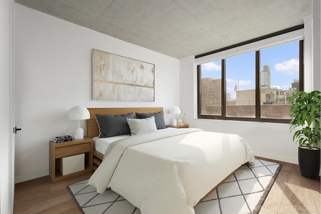 bedroom with wood finished floors, baseboards, and a city view