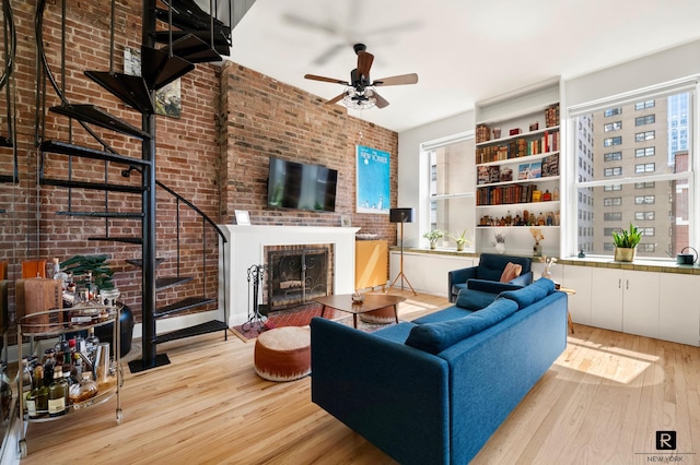 living room featuring a brick fireplace, wood finished floors, stairs, ceiling fan, and brick wall