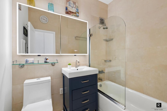 full bathroom featuring tile walls, combined bath / shower with glass door, vanity, and toilet