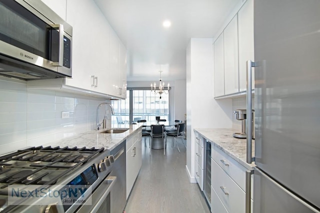 kitchen with appliances with stainless steel finishes, a sink, tasteful backsplash, light wood-style floors, and white cabinets