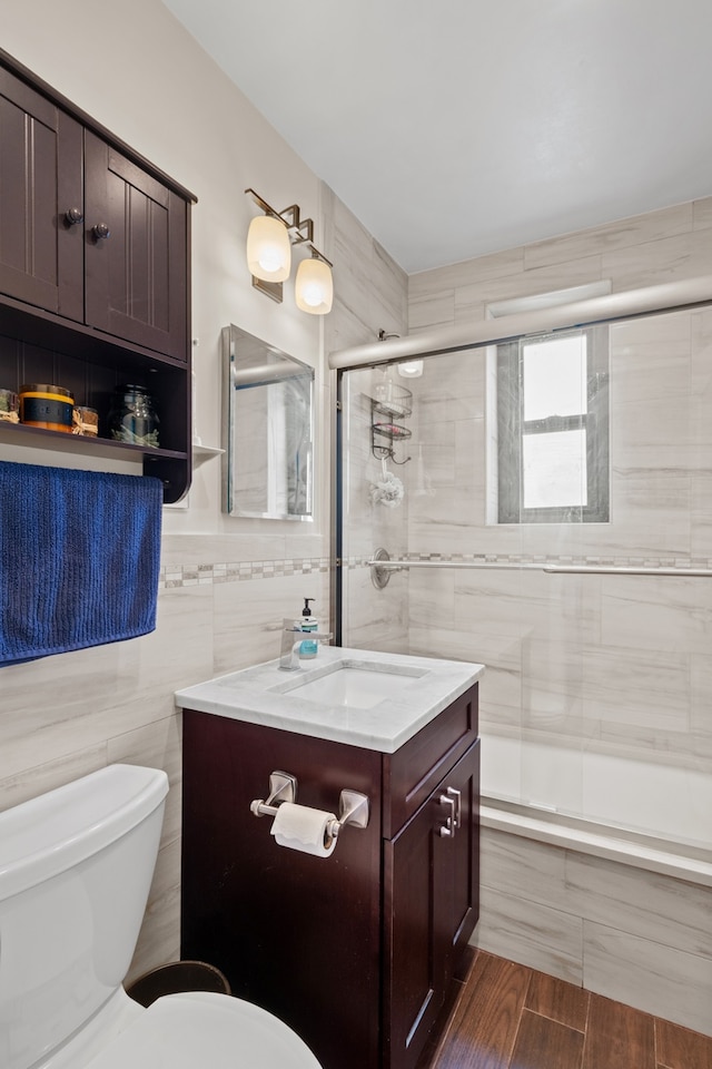 bathroom featuring tiled shower, tile walls, toilet, vanity, and wood finished floors