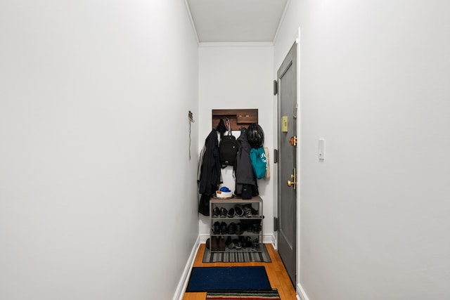hallway featuring wood finished floors, crown molding, and baseboards