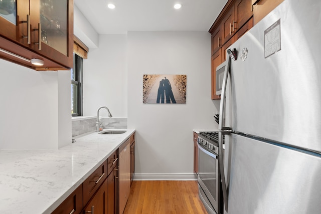 kitchen featuring appliances with stainless steel finishes, a sink, light wood-style floors, recessed lighting, and light stone counters