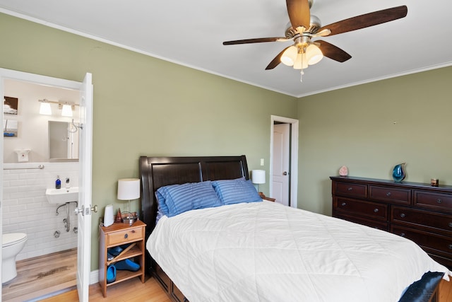 bedroom featuring light wood-style flooring, ornamental molding, ensuite bath, and a ceiling fan
