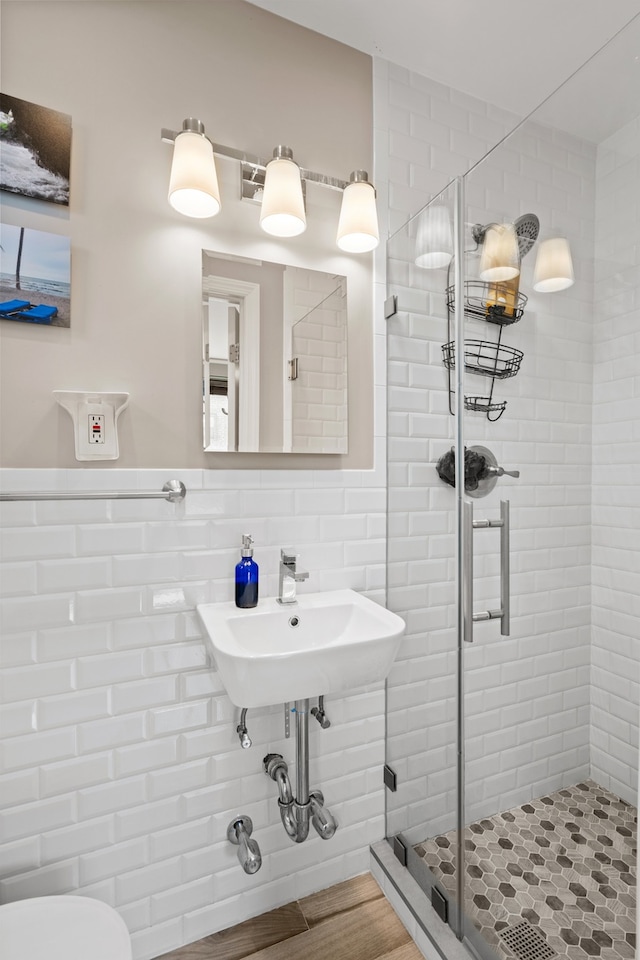 bathroom with a stall shower, tile walls, toilet, wainscoting, and wood finished floors