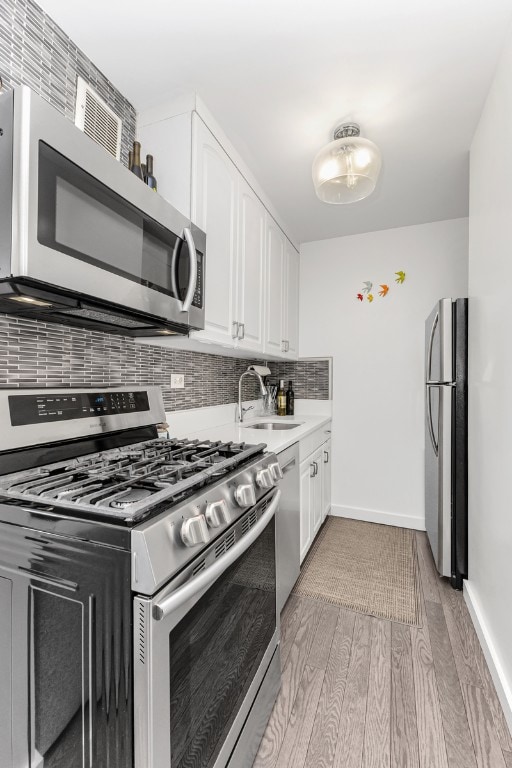 1641 3rd Ave Unit 28B, New York City, NY 10128 - kitchen featuring stainless steel appliances, backsplash, white cabinetry, and light wood-style floors
