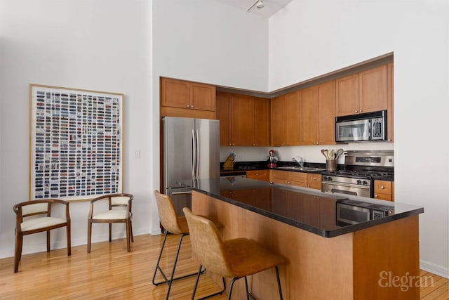 kitchen with appliances with stainless steel finishes, a towering ceiling, a sink, light wood finished floors, and a breakfast bar