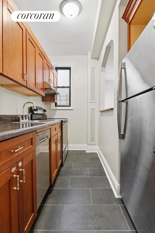 45 Martense St Unit 5L, New York City, NY 11226 - kitchen featuring appliances with stainless steel finishes, under cabinet range hood, brown cabinets, baseboards, and dark tile patterned floors
