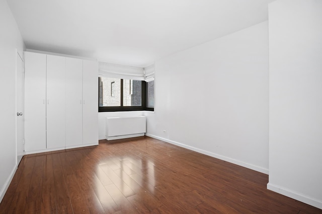 spare room featuring dark wood finished floors, baseboards, and radiator heating unit