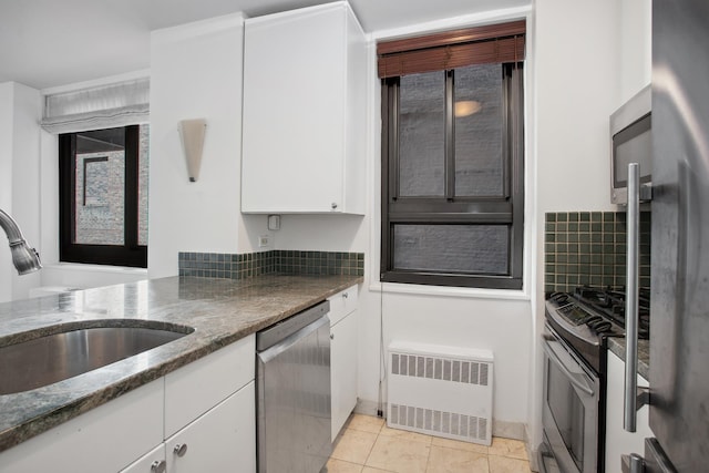 kitchen featuring stainless steel appliances, radiator, a sink, white cabinets, and dark stone counters