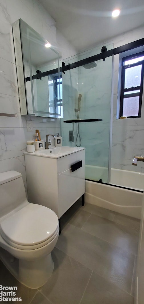 bathroom with plenty of natural light, toilet, enclosed tub / shower combo, tile patterned flooring, and tile walls