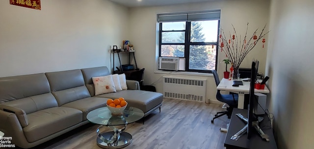 living area with radiator, healthy amount of natural light, wood finished floors, and cooling unit