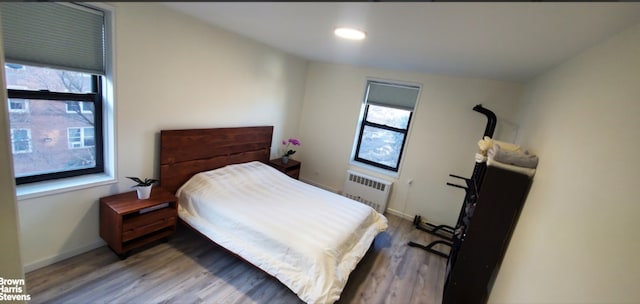 bedroom with radiator heating unit, multiple windows, wood finished floors, baseboards, and recessed lighting