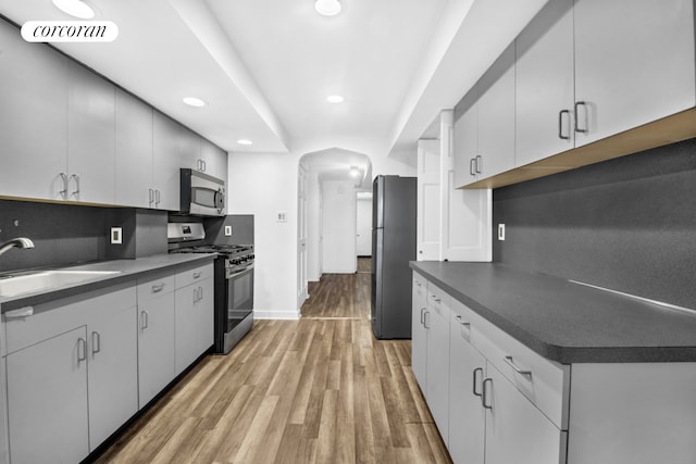 kitchen featuring stainless steel appliances, a sink, dark countertops, light wood-style flooring, and recessed lighting