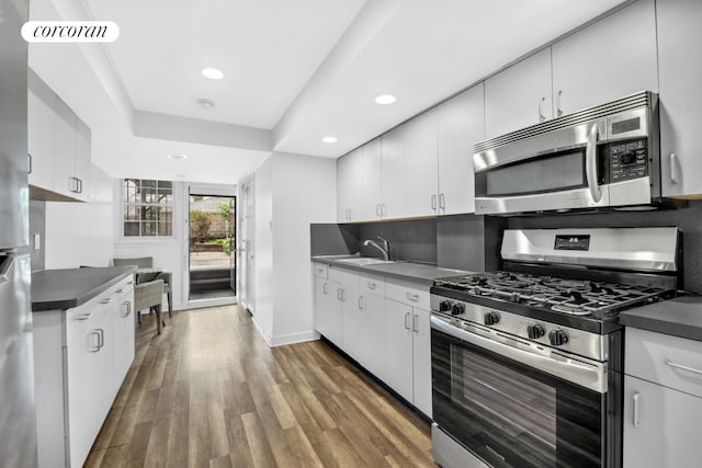 kitchen with stainless steel appliances, dark countertops, a sink, wood finished floors, and recessed lighting