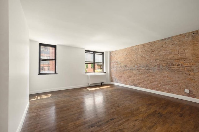 empty room with baseboards, dark wood-type flooring, and brick wall
