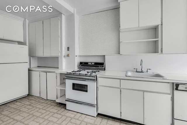 kitchen with white appliances, a sink, brick patterned floors, light countertops, and white cabinets