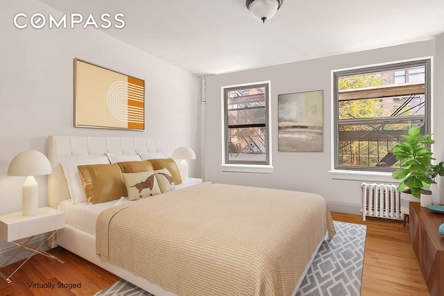bedroom with radiator heating unit, multiple windows, light wood-style flooring, and baseboards