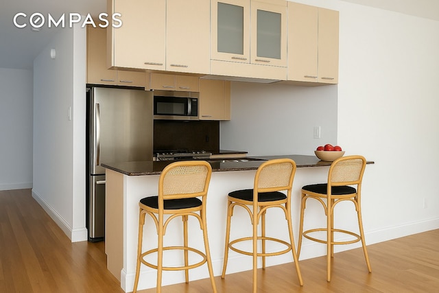 kitchen with stainless steel appliances, light wood-style flooring, baseboards, a peninsula, and glass insert cabinets