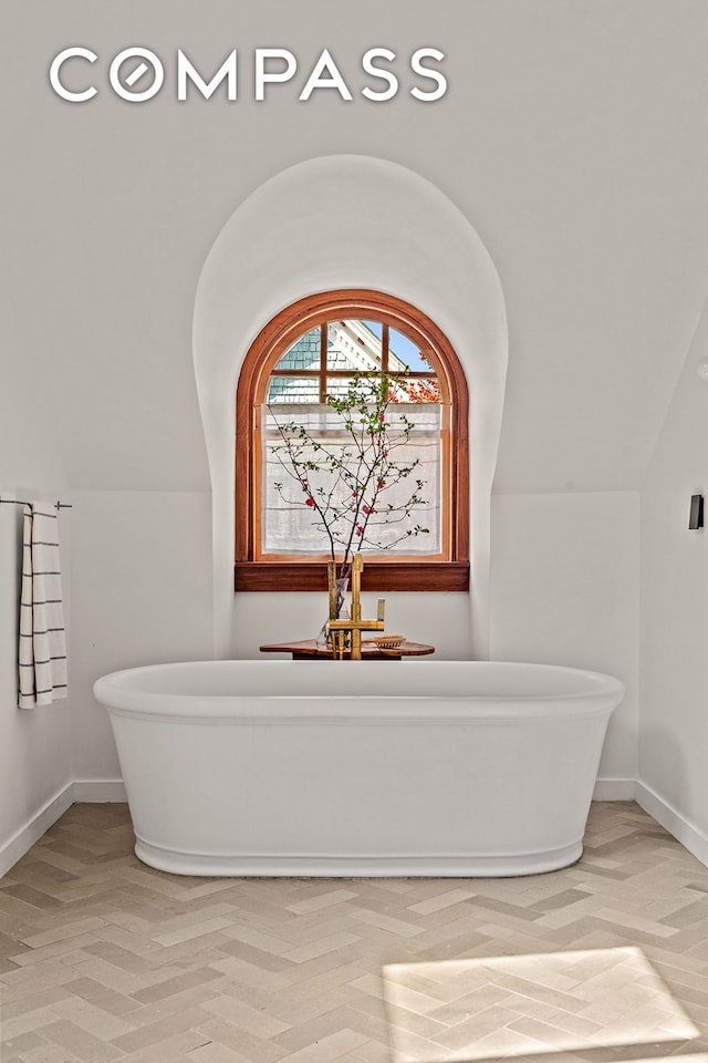 full bath with vaulted ceiling, baseboards, and a soaking tub
