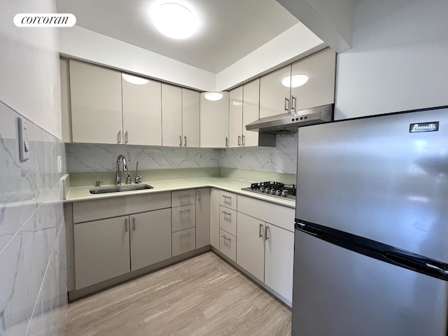 kitchen with stainless steel appliances, under cabinet range hood, a sink, light countertops, and light wood-style floors