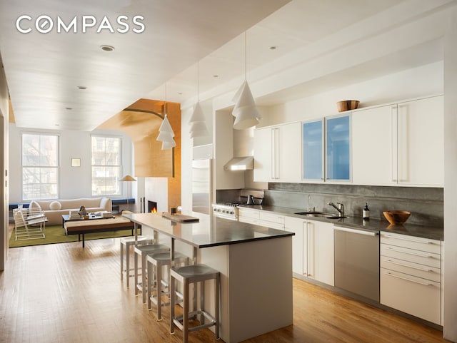 kitchen with high end appliances, a sink, dark countertops, a breakfast bar, and white cabinetry
