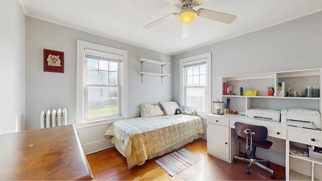 bedroom with radiator, multiple windows, wood finished floors, ornamental molding, and an office area