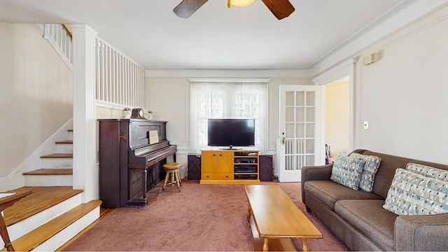 carpeted living room featuring ceiling fan and stairway
