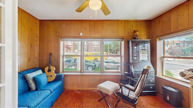 living area featuring wooden walls, carpet floors, and ceiling fan