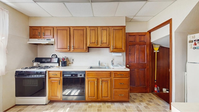 kitchen featuring white appliances, under cabinet range hood, light countertops, a sink, and wallpapered walls