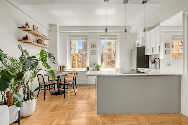 kitchen with freestanding refrigerator, a peninsula, hanging light fixtures, a sink, and white cabinets