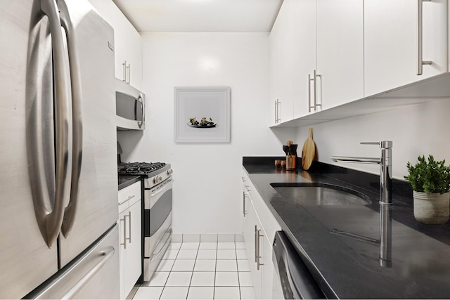 kitchen featuring stainless steel appliances, dark countertops, light tile patterned floors, white cabinetry, and a sink