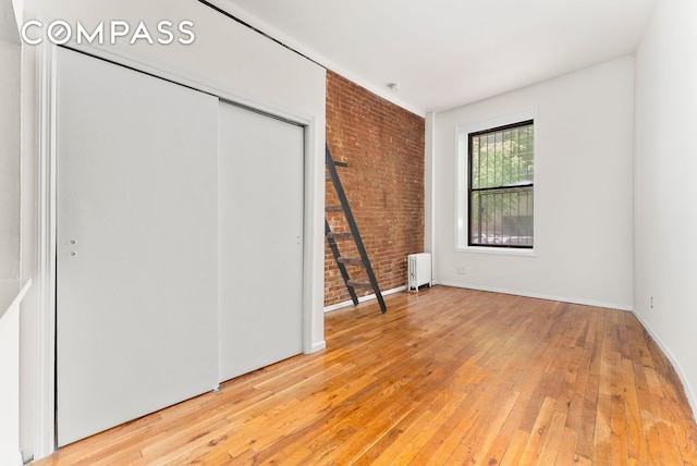 331 E 92nd St Unit 1A, New York City, NY 10128 - unfurnished bedroom with radiator heating unit, brick wall, light wood-style flooring, and a closet
