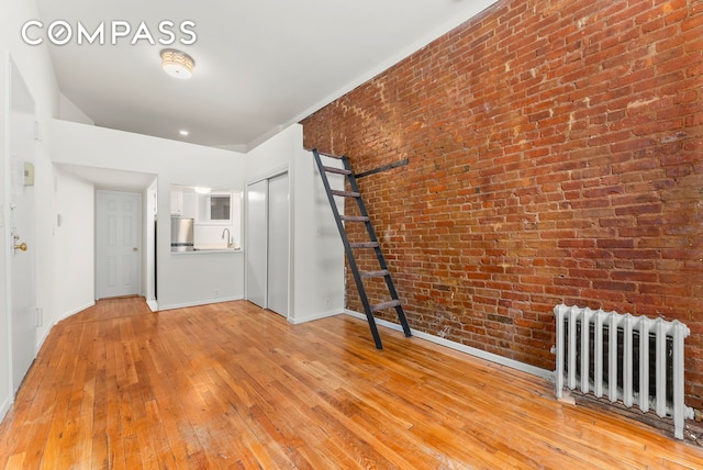 331 E 92nd St Unit 1A, New York City, NY 10128 - unfurnished living room with radiator, light wood-type flooring, and brick wall