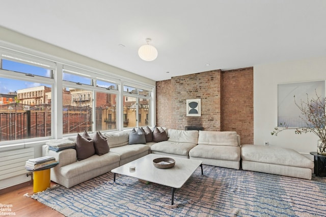 living room with healthy amount of natural light, brick wall, and wood finished floors