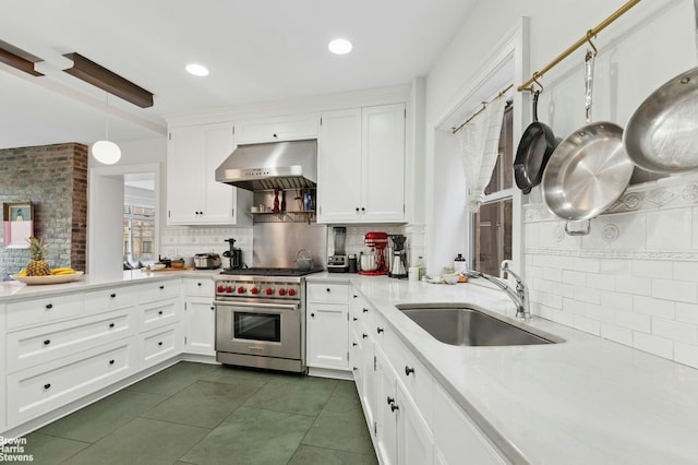kitchen with under cabinet range hood, luxury range, a sink, decorative backsplash, and light countertops