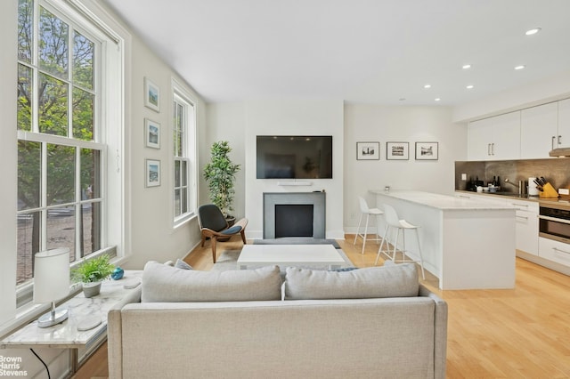 living area featuring healthy amount of natural light, light wood-style flooring, recessed lighting, and a fireplace with flush hearth
