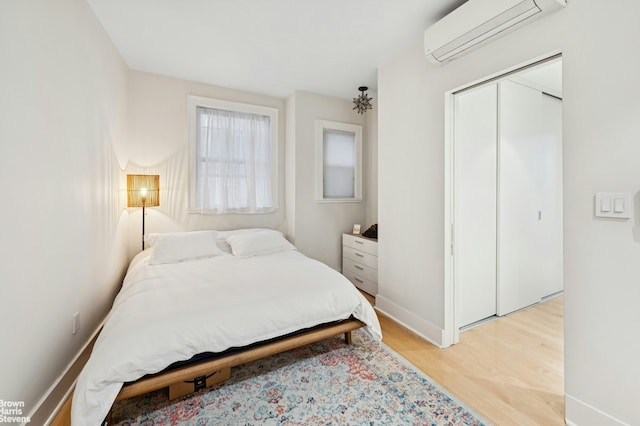 bedroom featuring a wall mounted AC, light wood finished floors, baseboards, and a closet