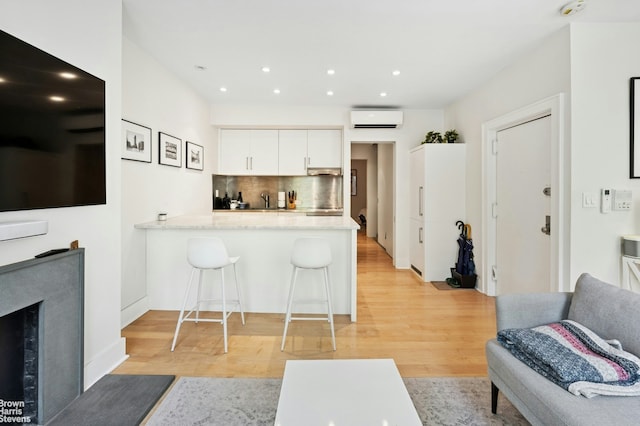living room featuring a wall mounted air conditioner, light wood-style flooring, and recessed lighting