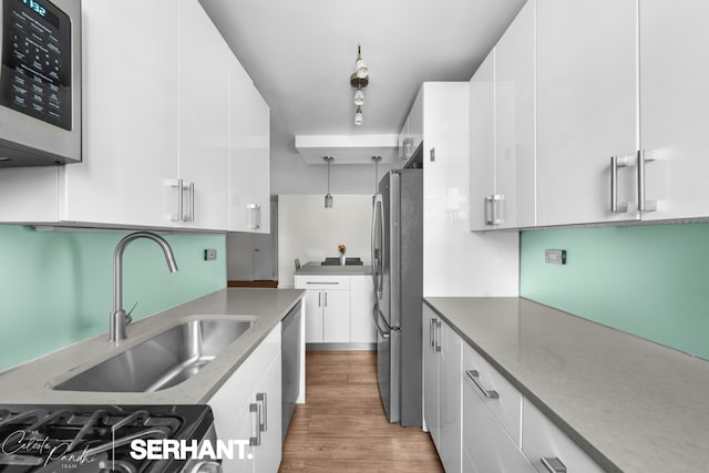 kitchen featuring stainless steel appliances, a sink, white cabinetry, light wood-style floors, and modern cabinets