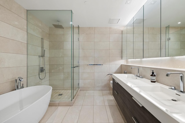 full bathroom featuring tile walls, a stall shower, a freestanding tub, tile patterned flooring, and double vanity