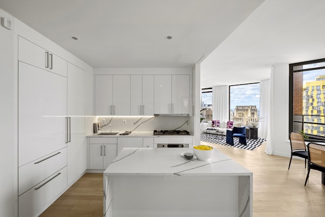 75 Wall St Unit Phl3, New York City, NY 10005 - kitchen featuring modern cabinets, light wood-style floors, white cabinetry, a sink, and a center island