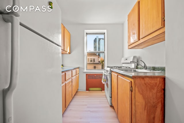 kitchen with freestanding refrigerator, gas range, a sink, light wood-type flooring, and brown cabinets
