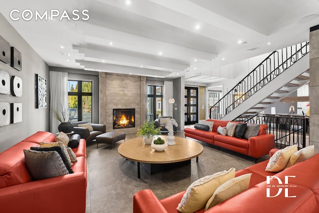 living room with finished concrete flooring, recessed lighting, a tile fireplace, and stairway