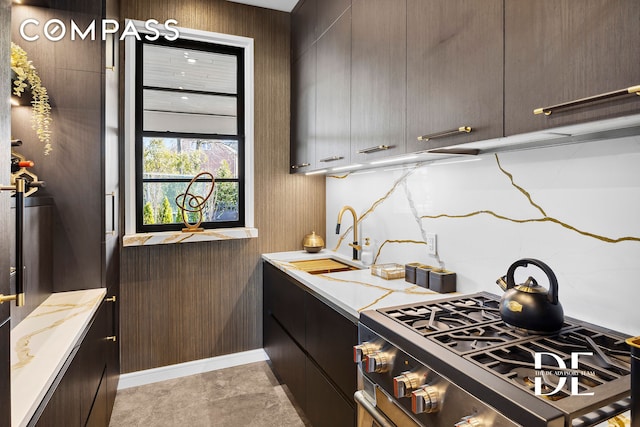 kitchen featuring stainless steel range with gas stovetop, a sink, dark brown cabinetry, and light stone countertops