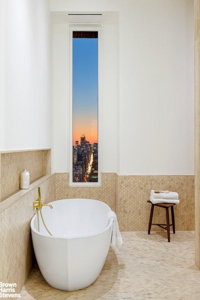 bathroom featuring a wainscoted wall, a soaking tub, and tile walls